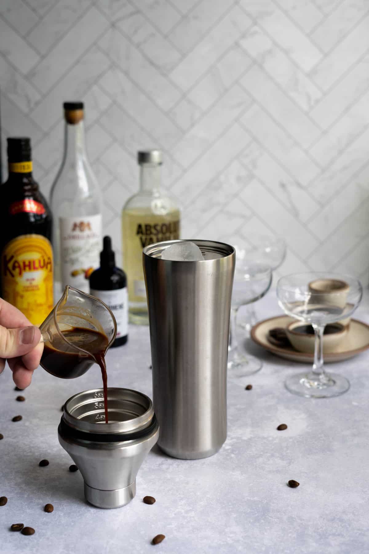 pouring espresso into a cocktail shaker to make a chocolate espresso martini.