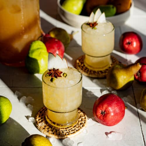 Two glasses of fall rum punch sit on a countertop surrounded by pears.