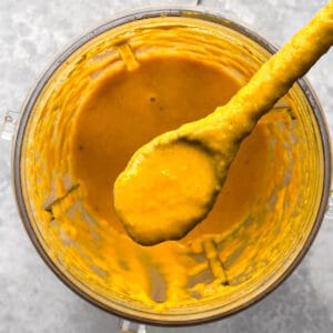 a spoonful of carrot ginger miso salad dressing is being scooped from the jar of a blender.