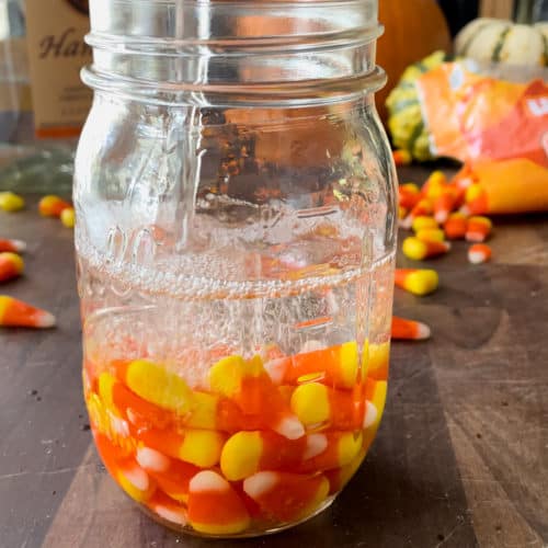 mason jar filled with candy corn with vodka poured into it for an infusion.