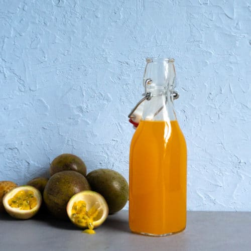 a glass bottle of passion fruit syrup sits next to a pile of passion fruits