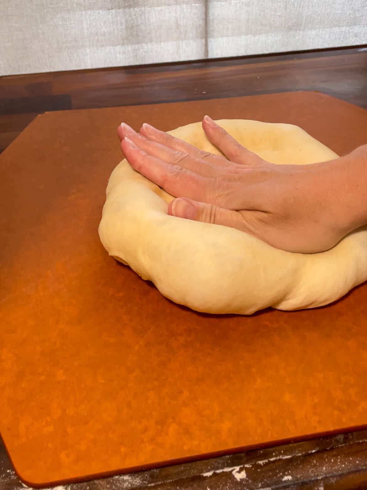 Shaping homemade pizza dough on a pizza peel using your hands.