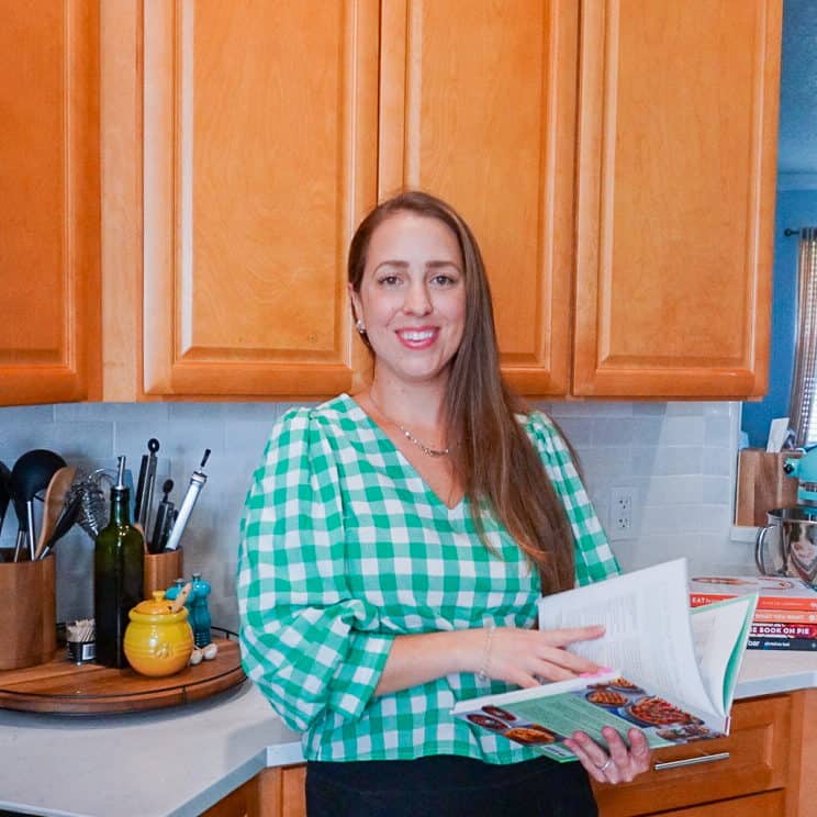 a female home chef named Lindsey standing in her kitchen leafing through a cookbook.
