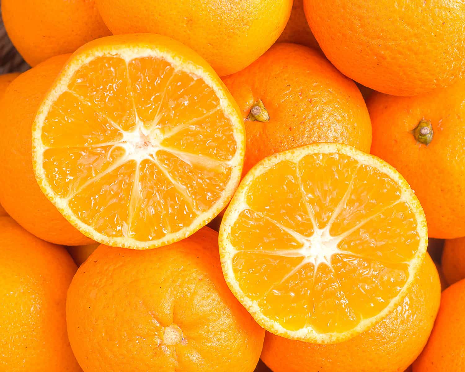 a group of oranges sits together in a photo with sliced oranges in the center of the frame.