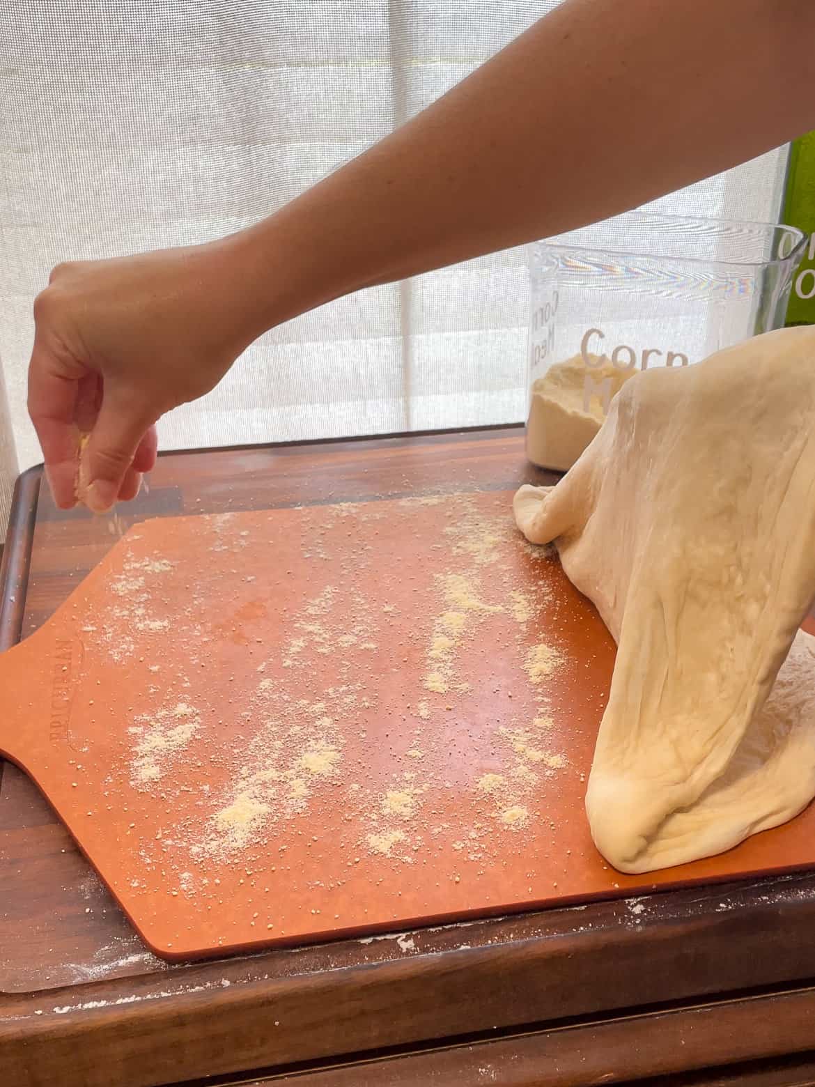 sprinkling cornmeal on a pizza peel while making homemade pizza dough