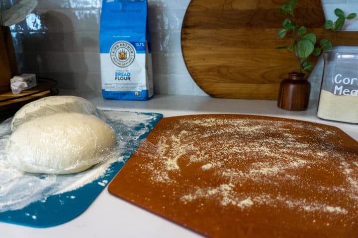 a prepared homemade pizza dough sits on the counter alongside the ingredients used to make it.