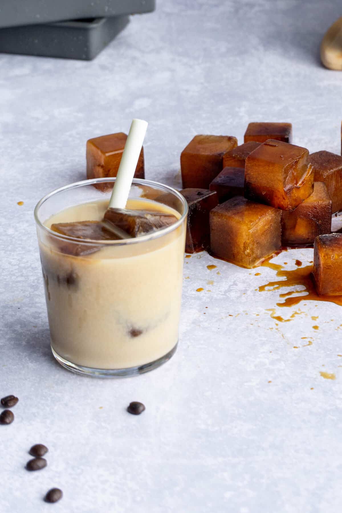 a glass of oat milk with espresso ice cubes sits on the countertop next to a pile of espresso ice cubes.
