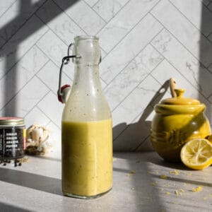 A bottle of freshly made lemon pepper dressing sits on a countertop at golden hour.