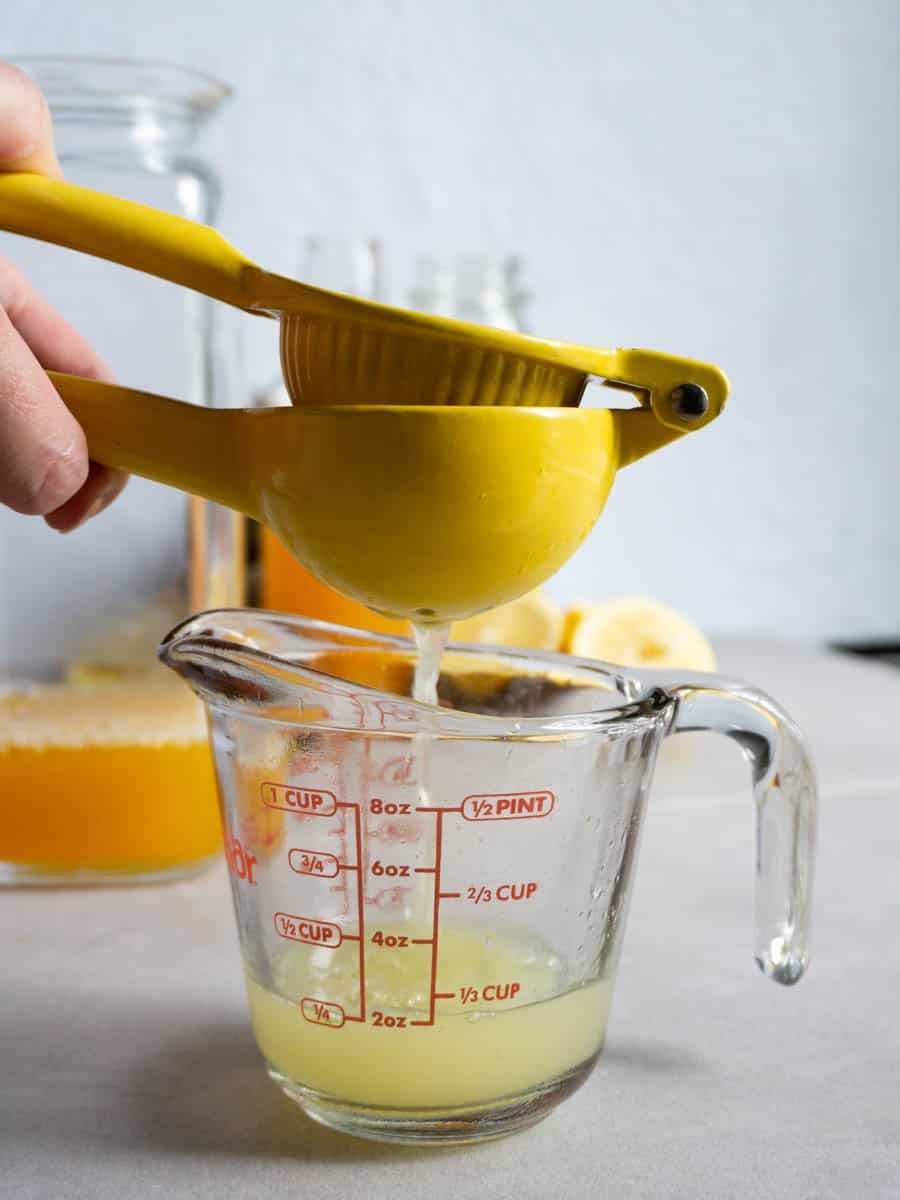 step 1 of making passion fruit lemonade: a lemon is being hand squeezed into a measuring cup to get 1 cup of lemon juice.