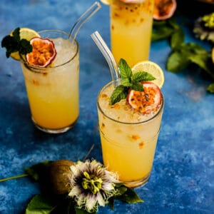 glasses of freshly made passion fruit lemonade are on a countertop next to a passion flower.