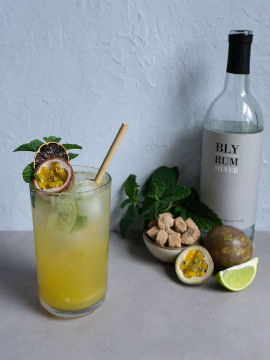 A passion fruit mojito sits on a countertop with the ingredients needed to make it in the background.