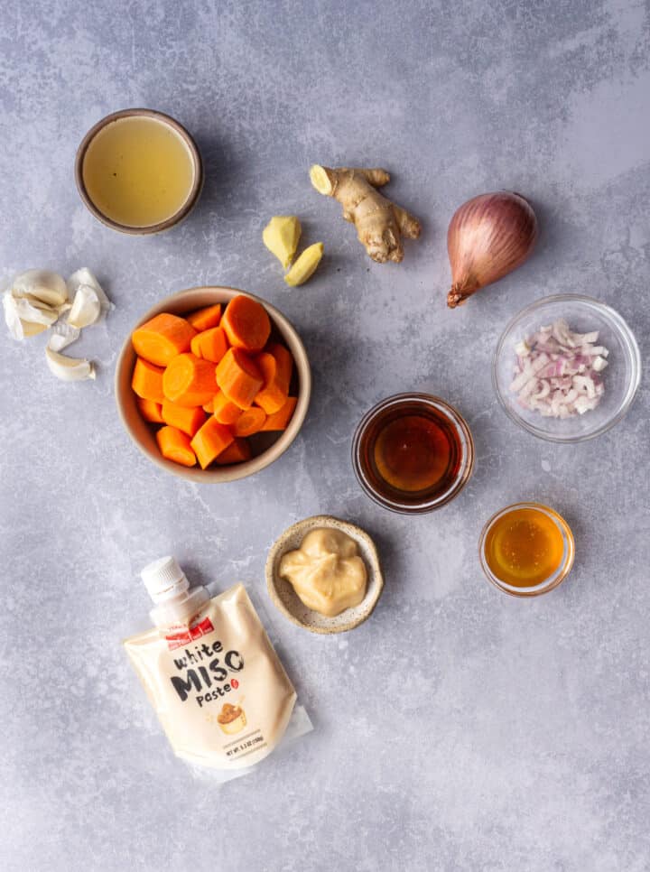 the ingredients for carrot ginger miso salad dressing are laid out on a countertop.