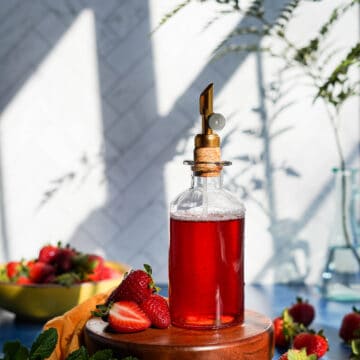 a bottle of strawberry simple syrup sits on a small pedestal.