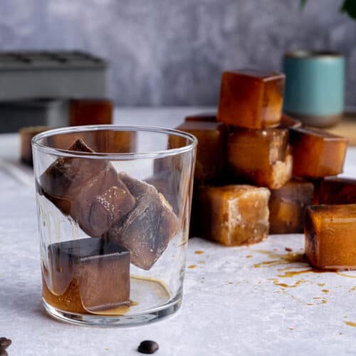 three espresso ice cubes are stacked in a glass in front of a pile of espresso ice cubes.