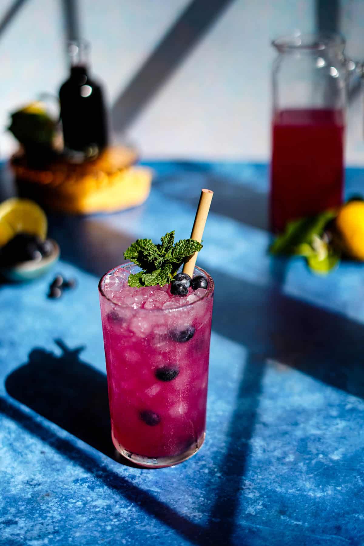 a glass of blueberry lemonade sits on a countertop in the sunlight.