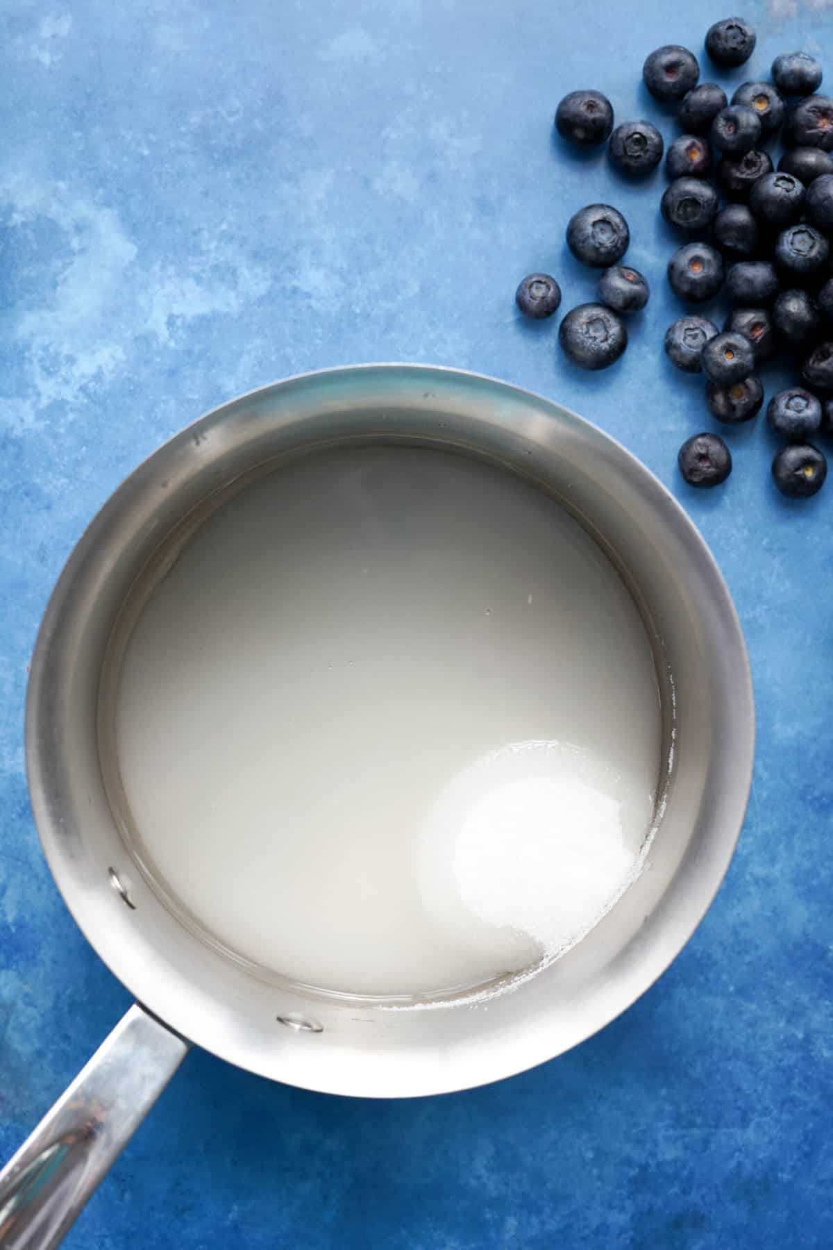 step one of making blueberry simple syrup: dissolving sugar into water in a small saucepan over medium-low heat.