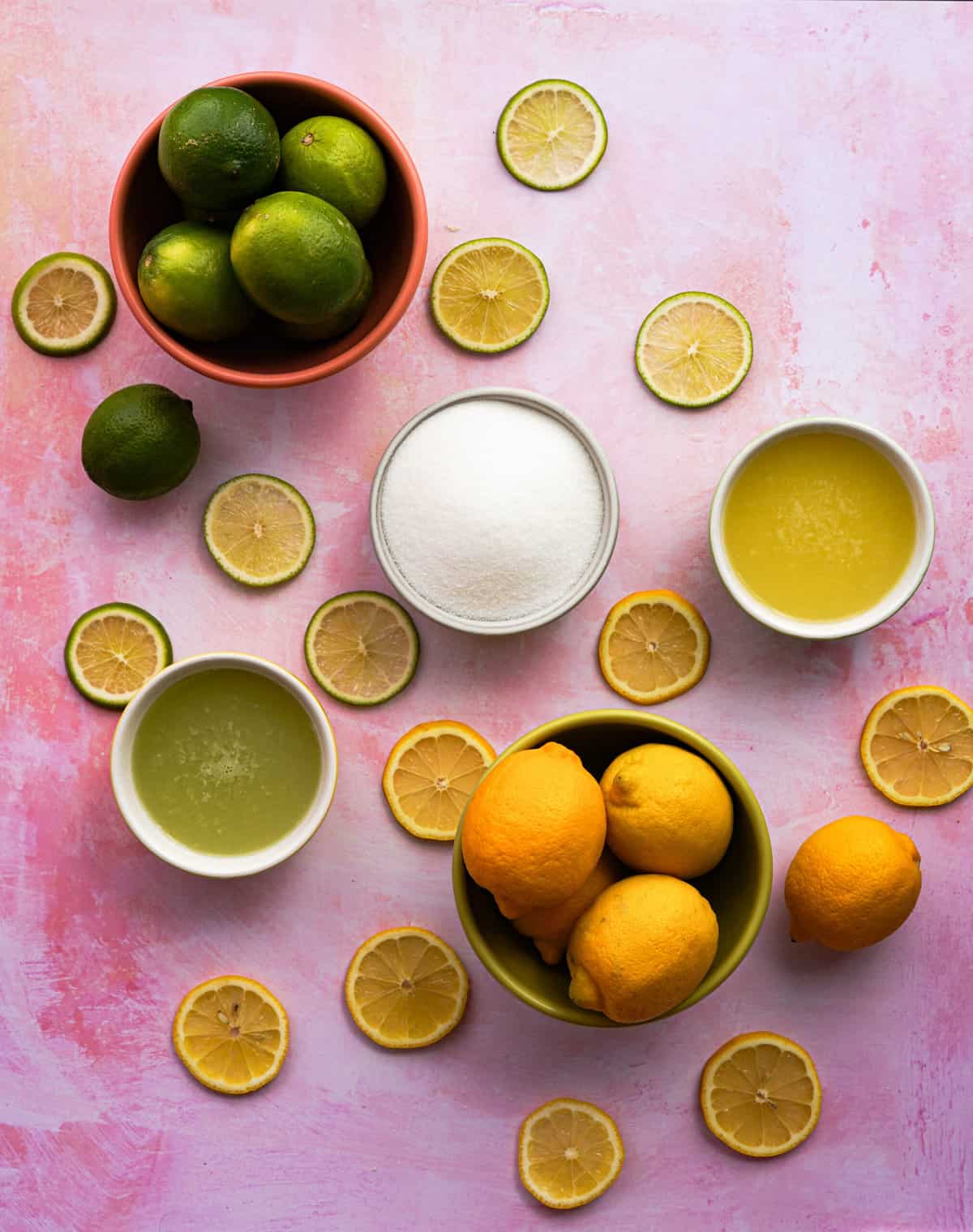 round slices of lemons and limes are scattered on a countertop alongside the rest of the ingredients to make a homemade sweet and sour mix recipe.