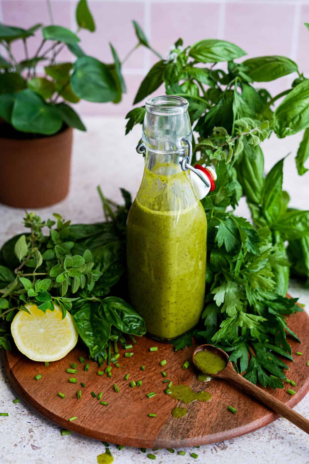 a bottle of simple herb vinaigrette sits on a round cutting board surrounded by herbs used to make the salad dressing.