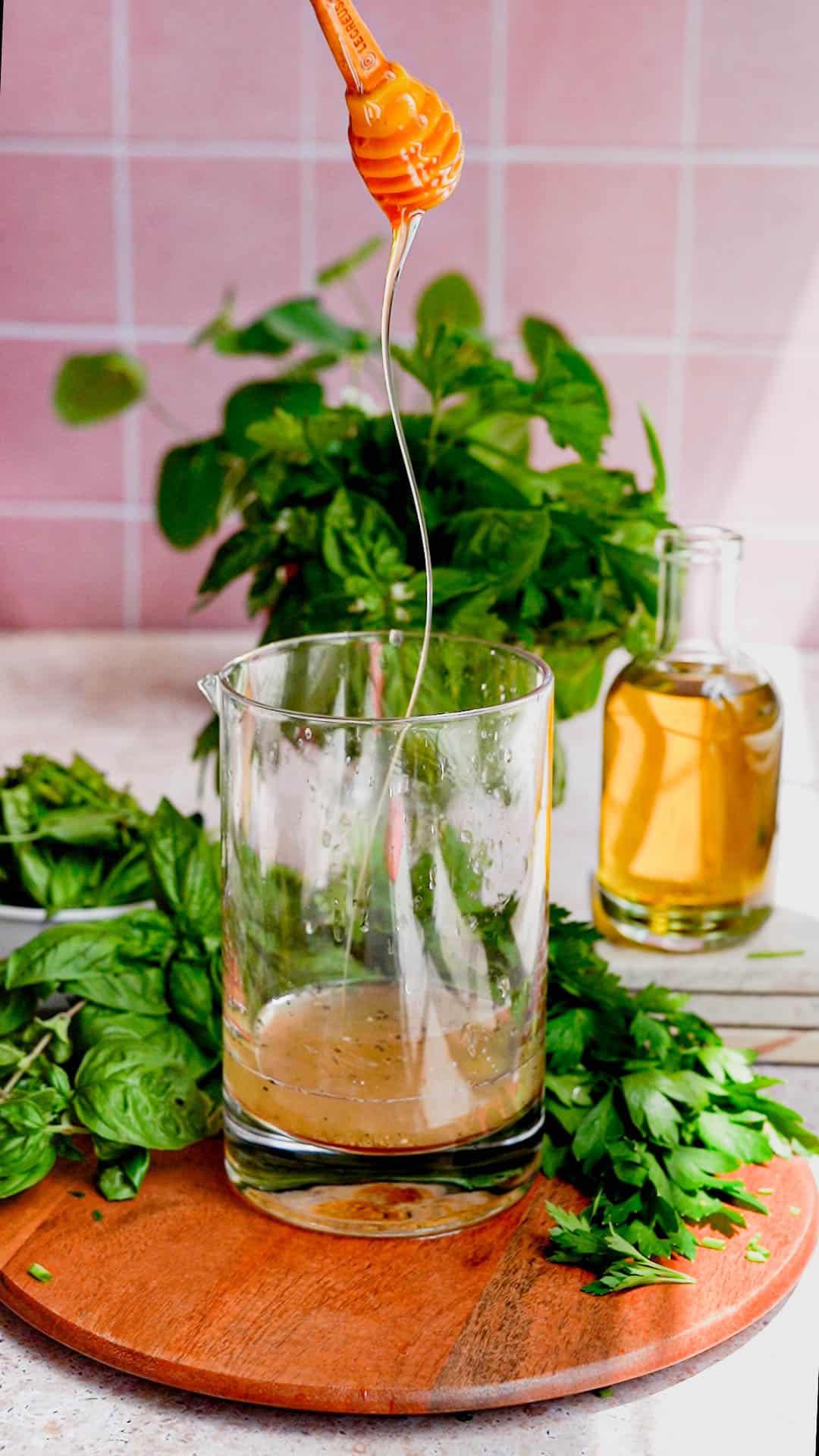 honey is being drizzled into a mixing glass filled with lemon juice and white wine vinegar to make a simple herb vinaigrette salad dressing.