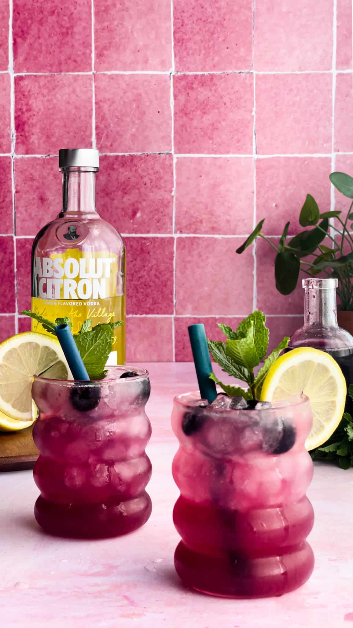 two sparkling blueberry vodka lemonade cocktails sit on a countertop, with a bottle of Absolute Citron in the background.