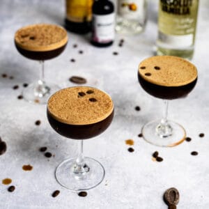 three chocolate espresso martinis sit on a messy marble countertop, with ingredients in the background.