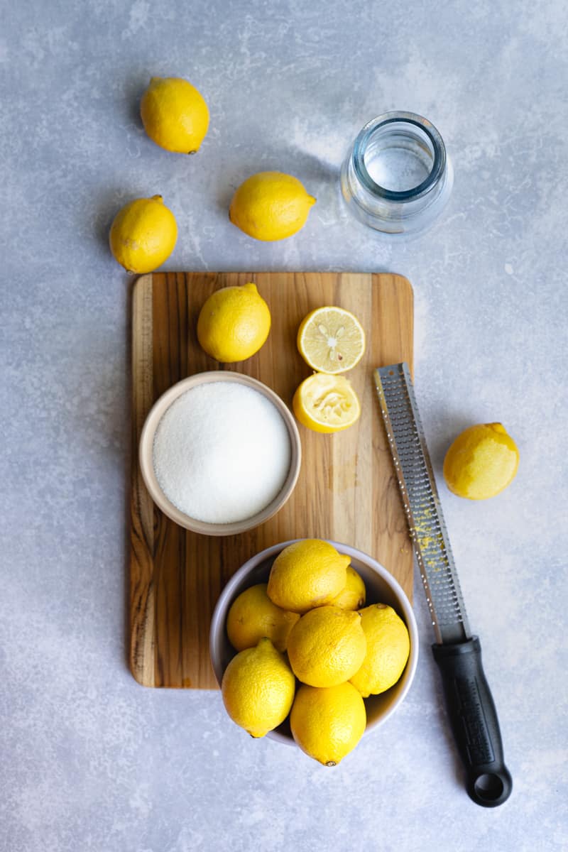 Ingredients used to make lemon simple syrup sit on a countertop. The ingredients include lemons, granulated sugar, and water.