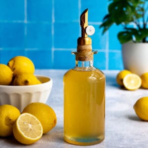 a bottle of bright yellow lemon simple syrup sits on a countertop to the right of a bowl of lemons.