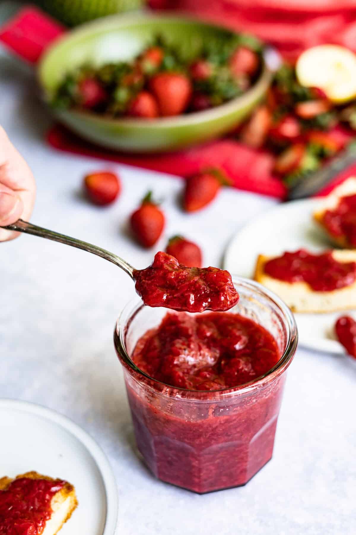 A spoon is being lifted from a jar of homemade strawberry jam. The strawberry jam was made without using pectin. 