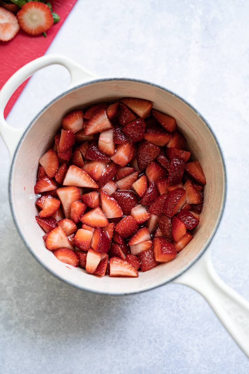 step five of making homemade strawberry jam without pectin: strawberries have been macerated with sugar, and they are glossy and almost soupy.