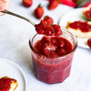 Feature image of strawberry jam without pectin. A spoon is being lifted from a jar of homemade strawberry jam. The strawberry jam was made without using pectin.
