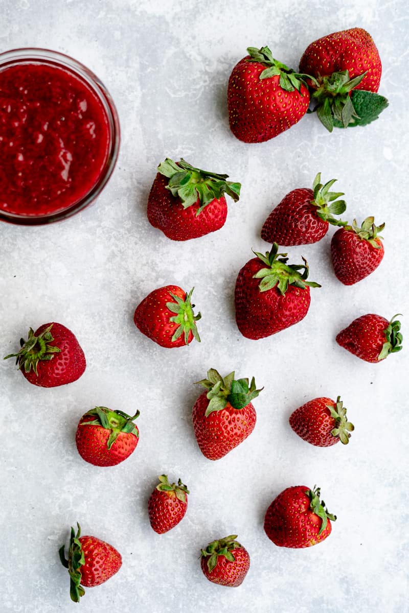 a countertop is scattered with strawberries, ranging in size and color, to show off the best berries to pick at the market. Smaller, deeper colored berries are the best choice for peak flavor. 