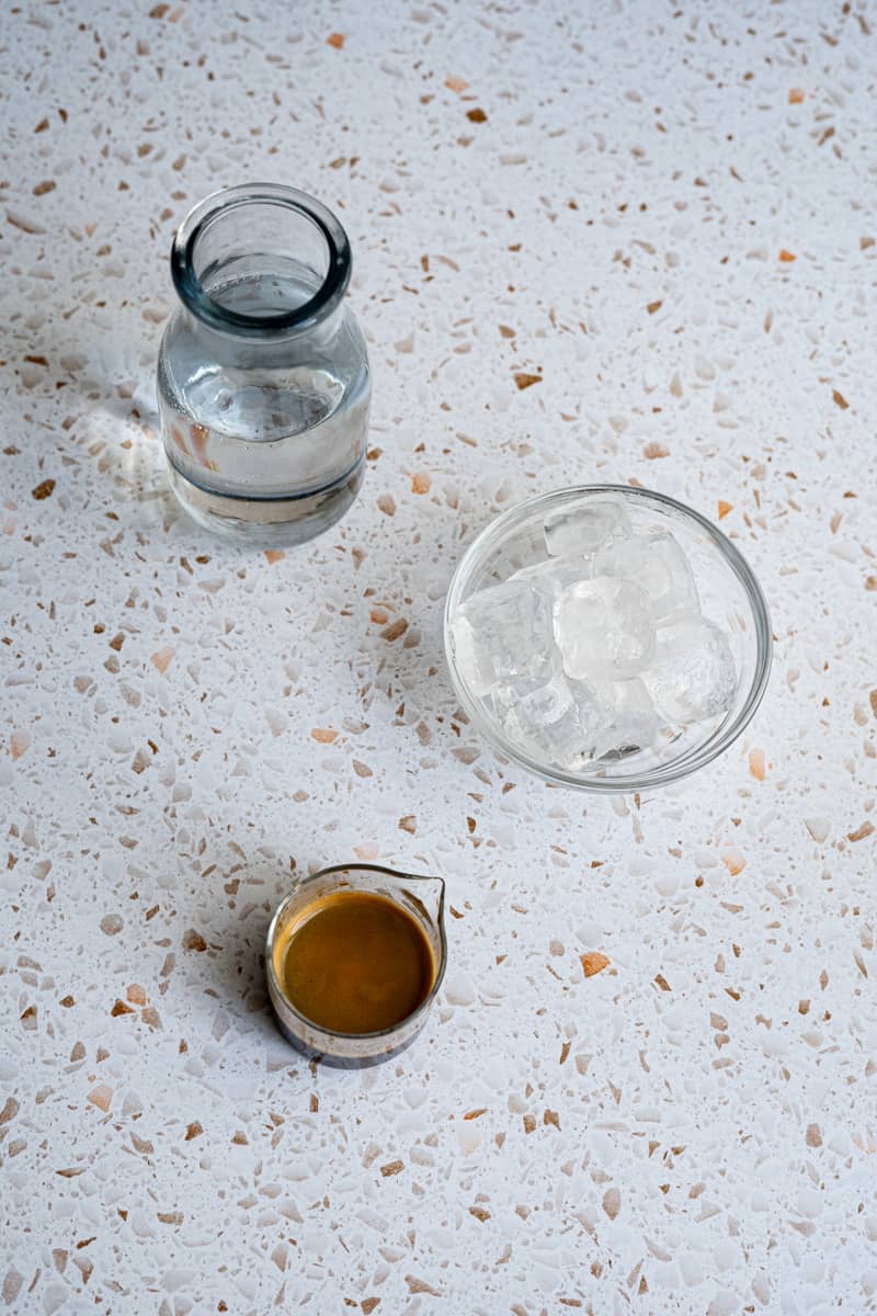 Ingredients used to make an Iced Americano coffee sit on a terrazzo countertop.