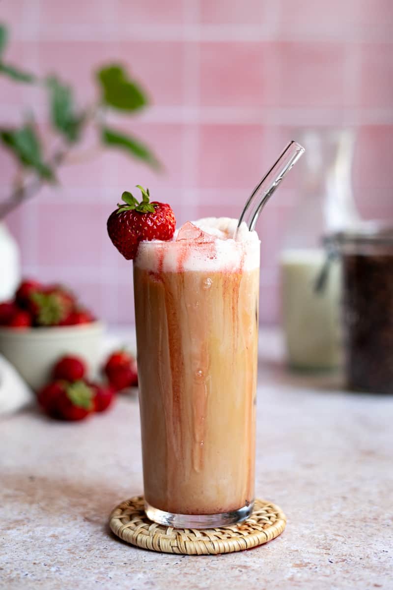 Feature image of a iced strawberry latte. Strawberry syrup and strawberry cold foam drip down the side of a glass filled with an iced strawberry latte.