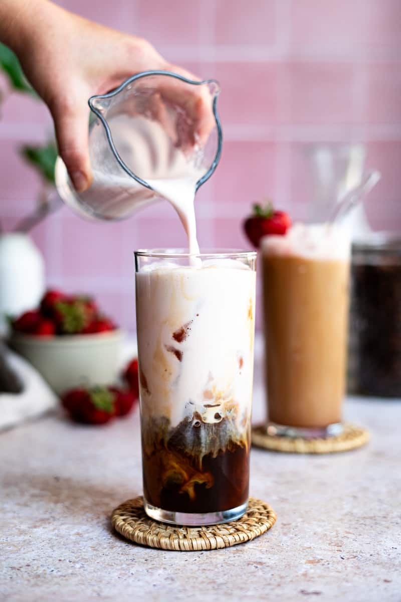 Step 7 of making an iced strawberry latte: Carefully layer the strawberry milk on top of the iced espresso.