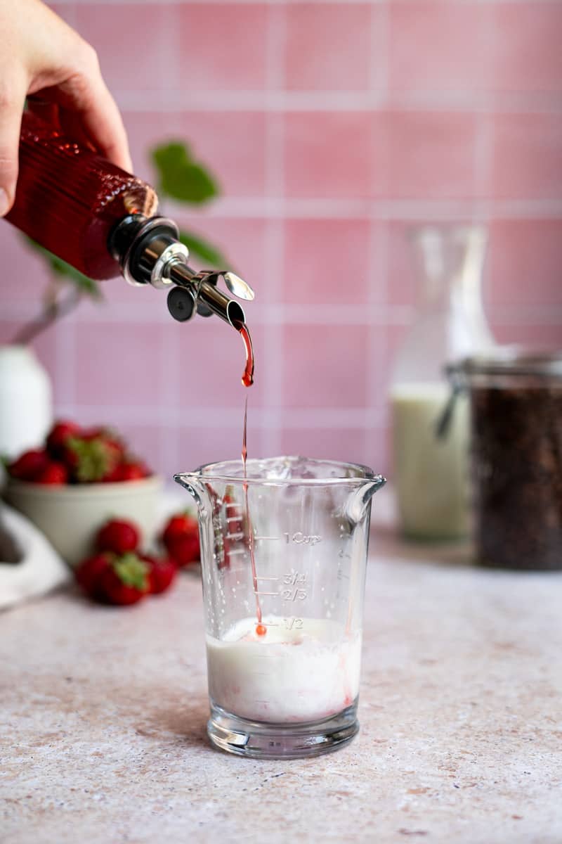 Step 4 of making an iced strawberry latte: Pour the strawberry simple syrup into the mixing glass with the milk.