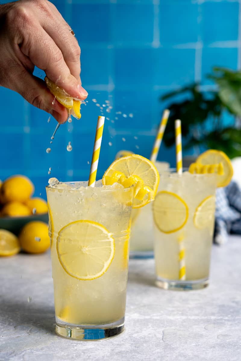 A hand from out of frame squeezes a slice of lemon onto a glass of freshly made Italian lemon soda pop, otherwise known as limonata.