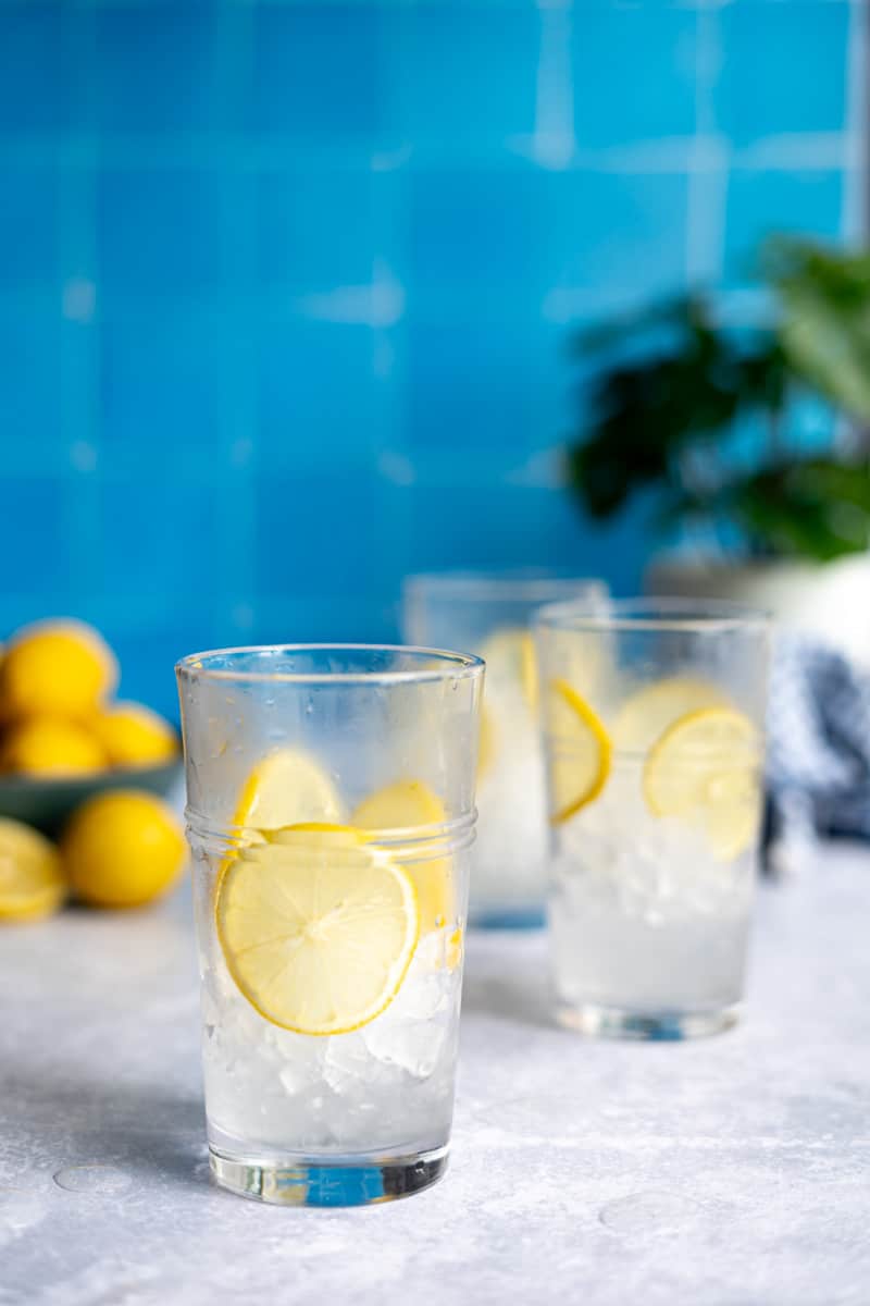 Step 2 of making a homemade lemon soda: fill a glass halfway with ice and garnish with lemon slices.