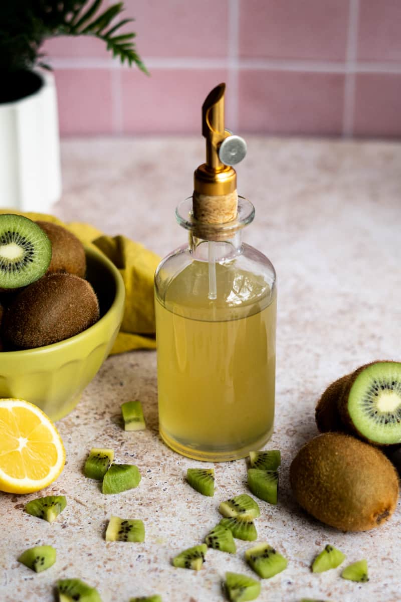 kiwi simple syrup sits on a countertop in a bottle with a gold pour spout.