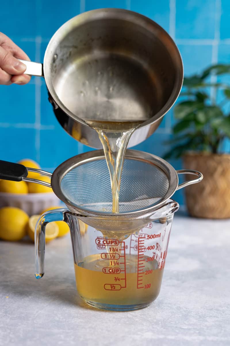 Step 7 of making homemade lemon simple syrup: straining the syrup through a fine mesh strainer.