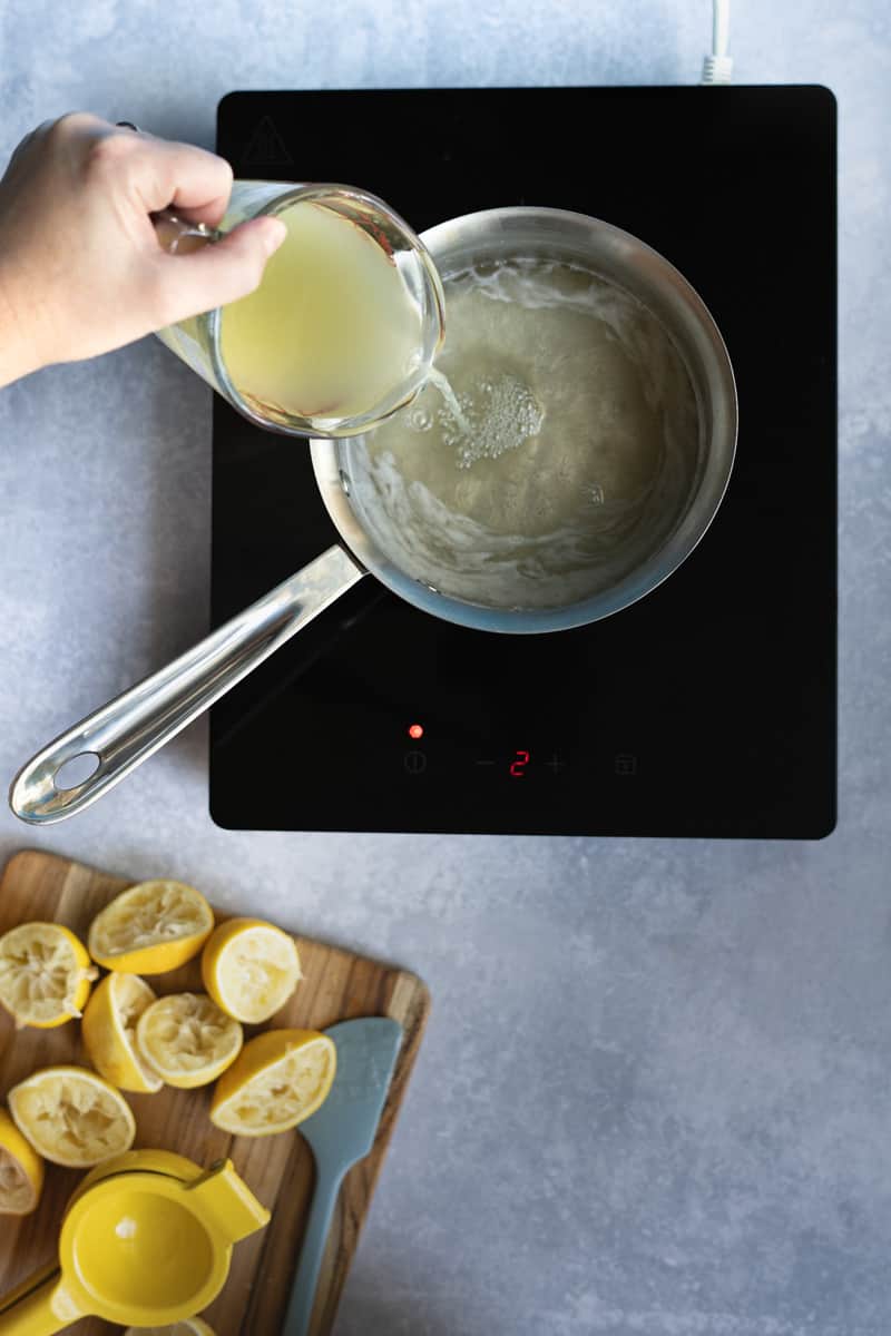 Step 5 of making homemade lemon simple syrup: adding lemon juice to the simple syrup and allowing it to simmer for 15-20 minutes.