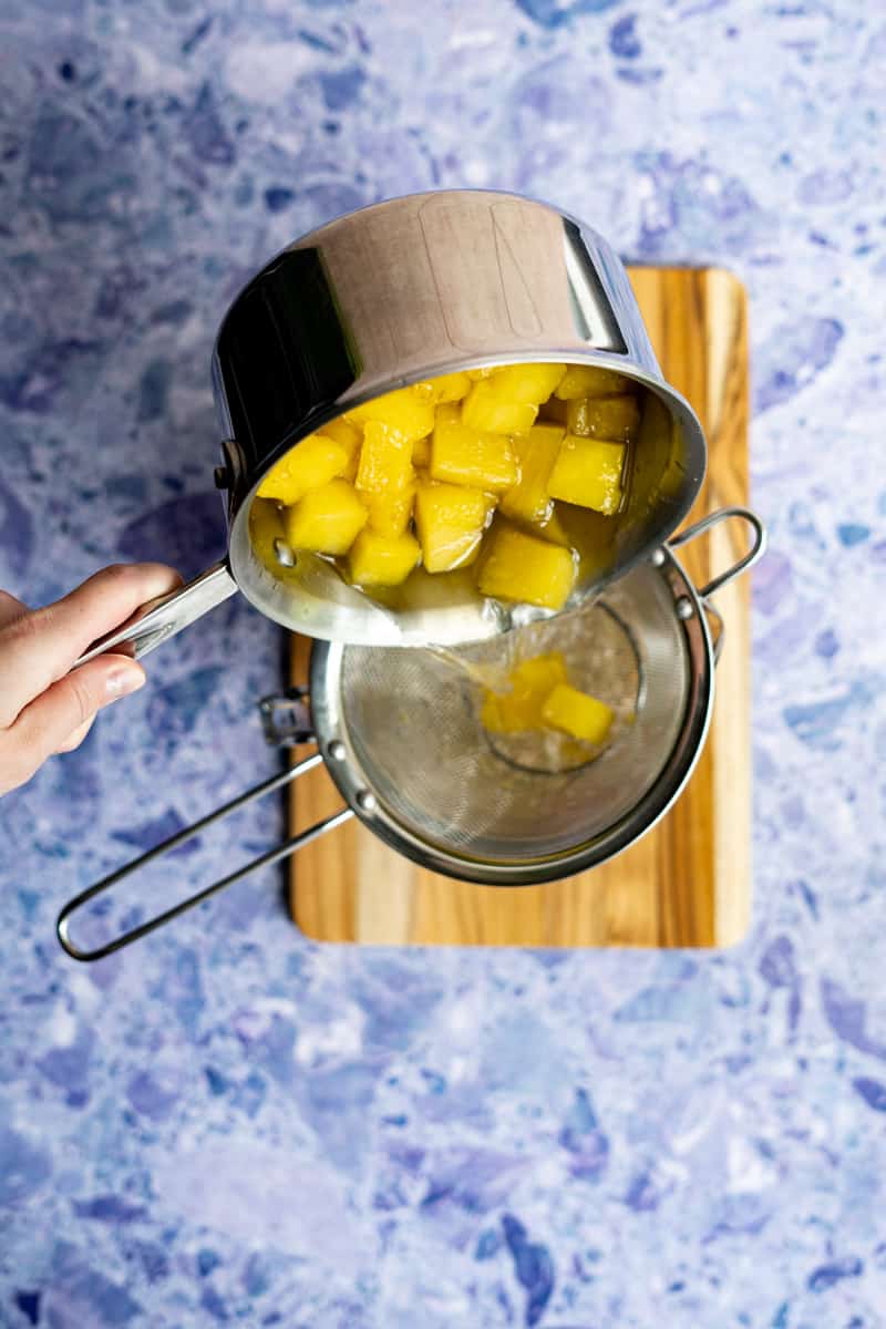 step 9 of making pineapple simple syrup: straining the syrup using a fine mesh strainer.