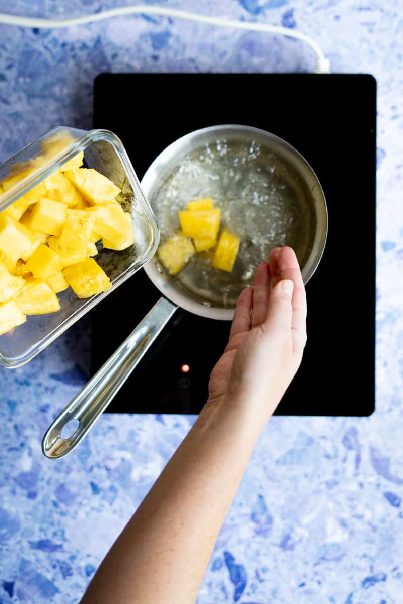 step 6 of making homemade pineapple syrup: adding in pineapple chunks.
