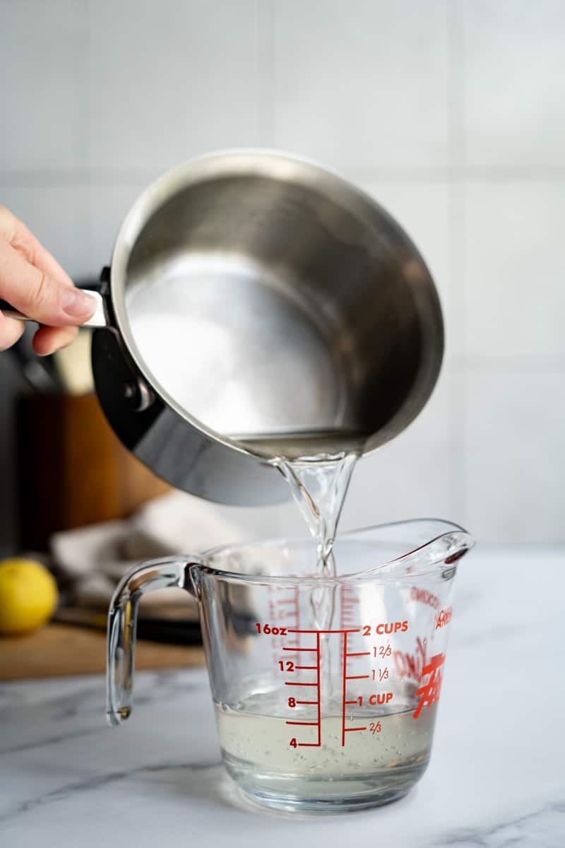 Transferring the simple syrup to a heat-safe container to pour it into a storage container.
