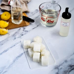 Feature image for a post about whether or not you can freeze simple syrup for storage. A pile of simple syrup ice cubes sits on a counter top next to ingredients that were used to make the syrup.