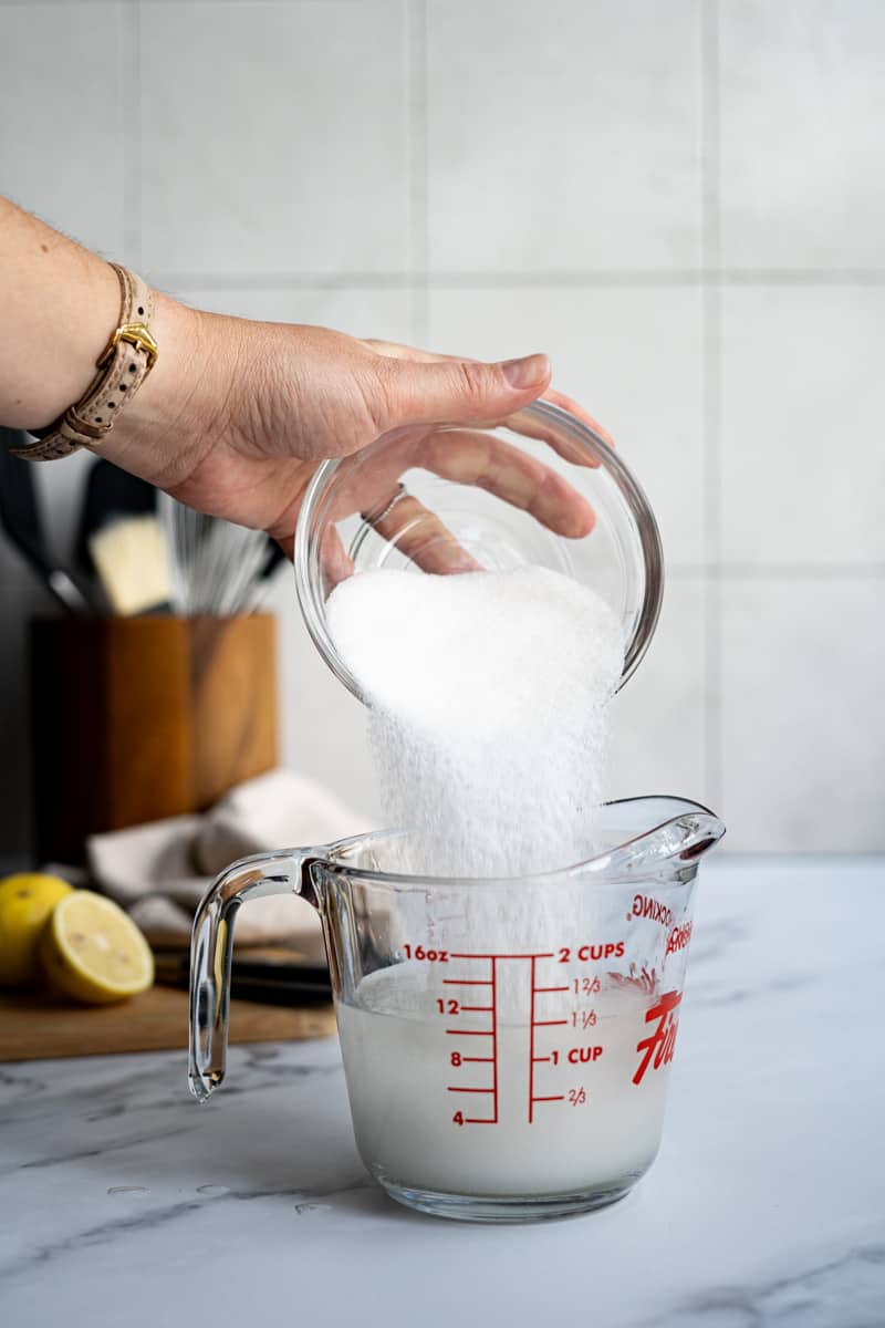Adding sugar to the measuring glass to make simple syrup at room temperature.