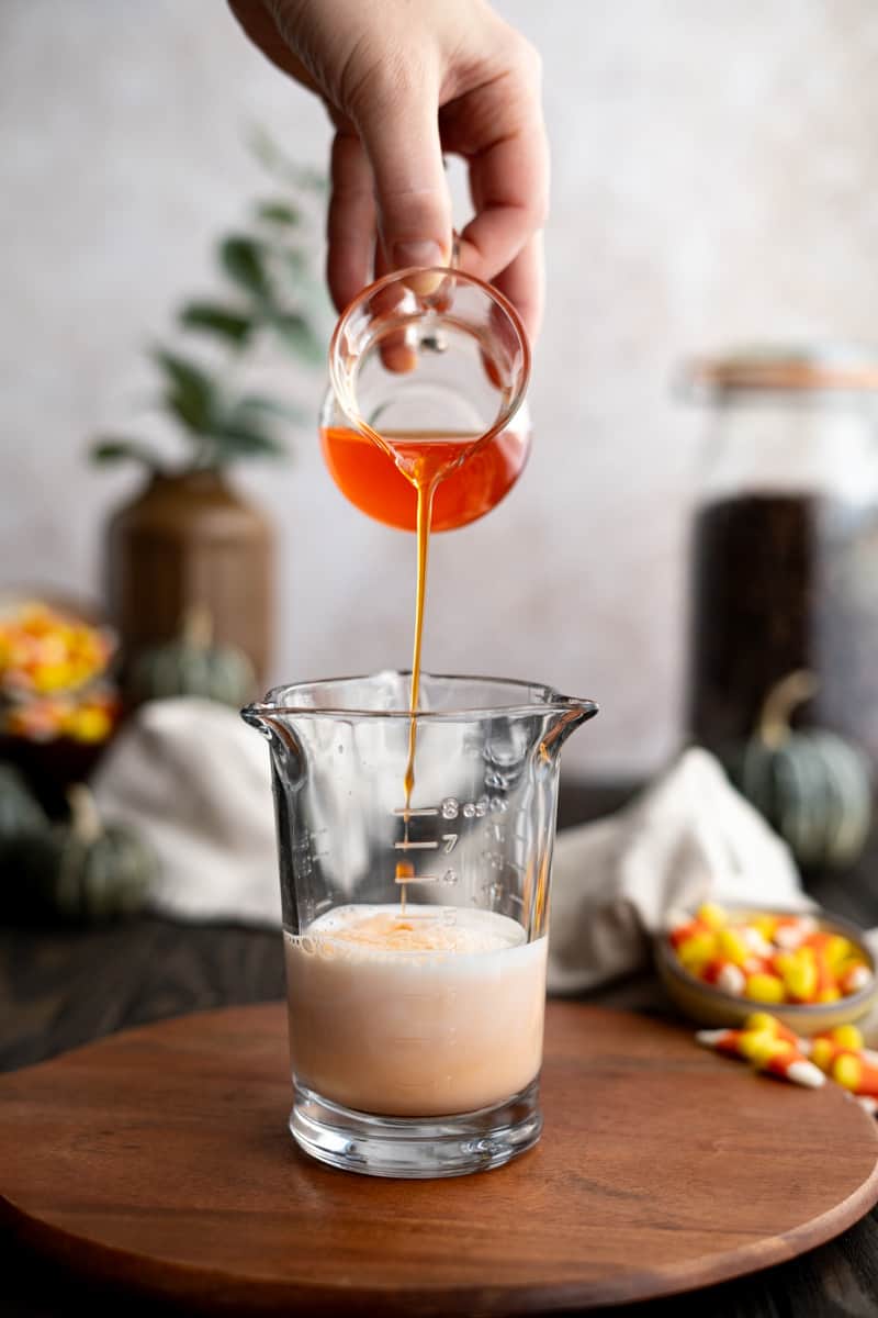 Candy corn simple syrup is being added to the milk in a mixing glass.