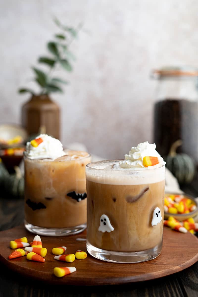Two candy corn lattes sit on a countertop garnished with whipped cream and candy corn.
