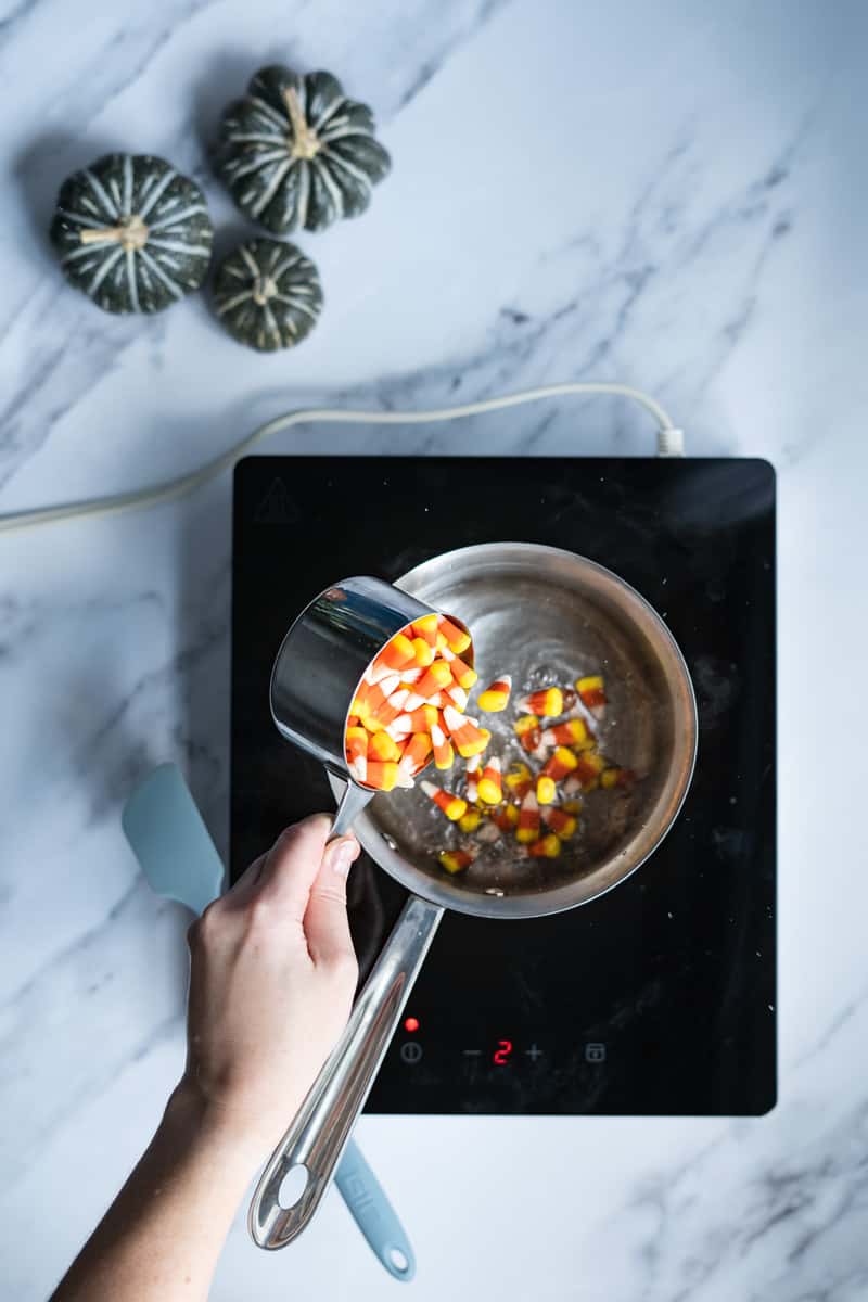 Step 2 in making candy corn simple syrup: pouring candy corn into the heated water.