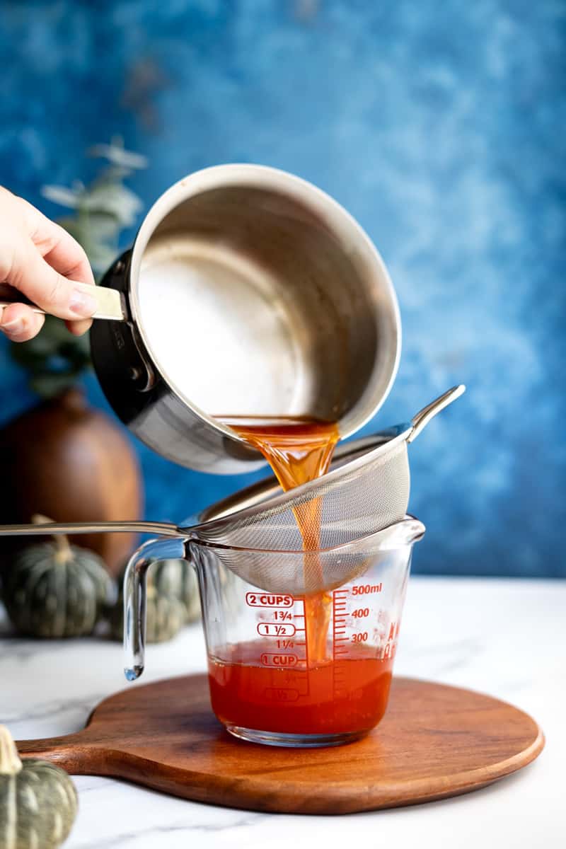 Pouring a candy corn simple syrup through a fine mesh sieve.