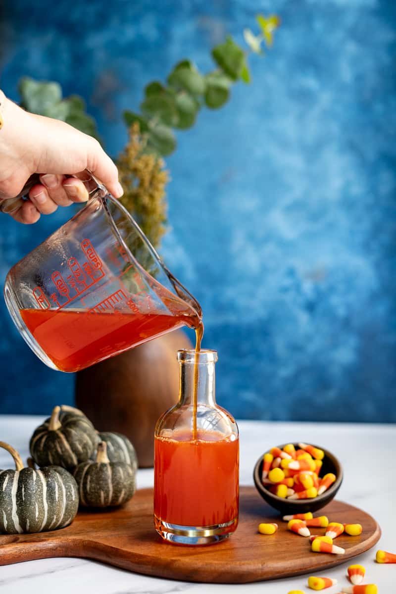 Pouring candy corn simple syrup into a storage bottle.
